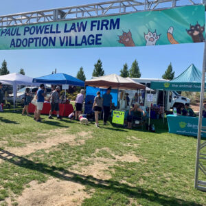 Outdoor event featuring the Paul Powell Law Firm's Adoption Village, with tents, people, and animal rescue organizations, promoting animal adoption and personal injury legal services in Las Vegas.