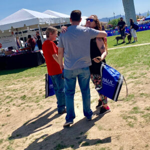 People at a Las Vegas community event, possibly related to pet care, with one person hugging another while holding a blue bag with a law firm logo, potentially promoting legal services for personal injury claims.