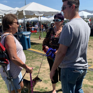 Three people chat at an outdoor event in Las Vegas, one with a mobility aid and a dog, highlighting community engagement and support for individuals navigating personal injuries.