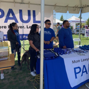 A promotional booth for a Las Vegas personal injury law firm featuring branded materials and staff at an outdoor event, with attendees and promotional items visible.