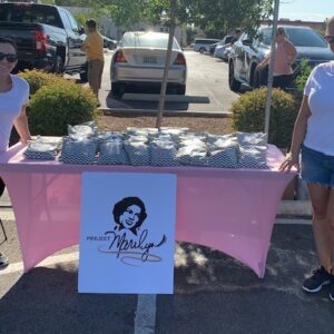 Two women stand behind a pink table at an outdoor event with Project Marilyn branding, promoting community support and legal services for personal injury cases in Las Vegas.