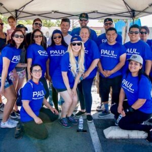 A group of smiling people wearing blue t-shirts with "PAUL. More Lawyer. Less Fees." are standing together for a team photo at a Las Vegas law firm specializing in personal injury cases.