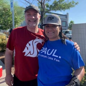 Two smiling individuals, one wearing a shirt promoting "Paul, More Lawyer, Less Fee," stand outdoors, suggesting a community event supported by a Las Vegas personal injury law firm offering accessible legal services.