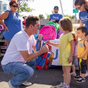 Image shows a law firm in Las Vegas giving away backpacks to children at a community event, showcasing their commitment to personal injury victims and the local community.