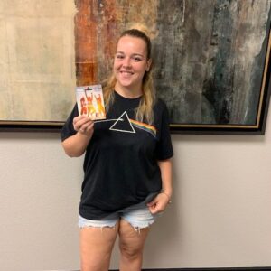 A smiling woman in a 'Dark Side of the Moon' t-shirt holds up a Visa gift card with an image of people celebrating, possibly a client who received compensation from a personal injury case handled by a Las Vegas law firm.