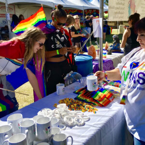 A Las Vegas personal injury law firm demonstrates community support at an outdoor event with pride flags, mugs with 'Love Wins' slogans, and rainbow-themed merchandise.