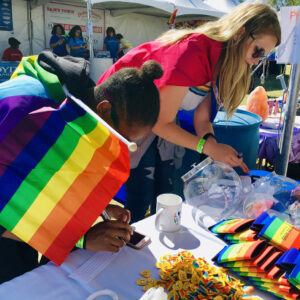 A personal injury law firm in Las Vegas supports diversity by participating in a community event, with two women signing up for a raffle near rainbow flags, emphasizing the firm's commitment to equality and justice.