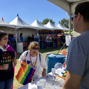 Outdoor event featuring people at a booth with rainbow flags and LGBTQ+ themed merchandise; could be used for personal injury if an accident occurred at a similar event.