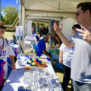 A law firm booth at a Las Vegas Pride event features volunteers, rainbow flags, and promotional merchandise, highlighting their commitment to inclusivity and support for personal injury clients within the LGBTQ+ community.