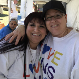 Two smiling women at a community event, representing a Las Vegas personal injury law firm, wearing "Love Wins" shirts, showing support and solidarity.