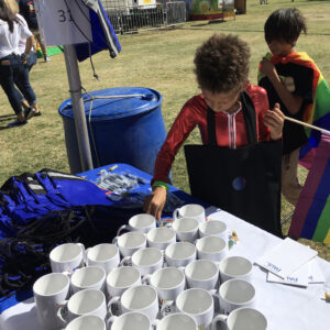 A law firm at a local community event in Las Vegas, offering promotional items like mugs and bags, with children nearby holding a rainbow flag, symbolizing support and inclusivity.