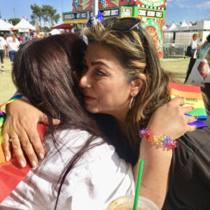 Two women embracing at an outdoor event with "Love Wins" in hand, symbolizing support and understanding for those facing personal injury claims.
