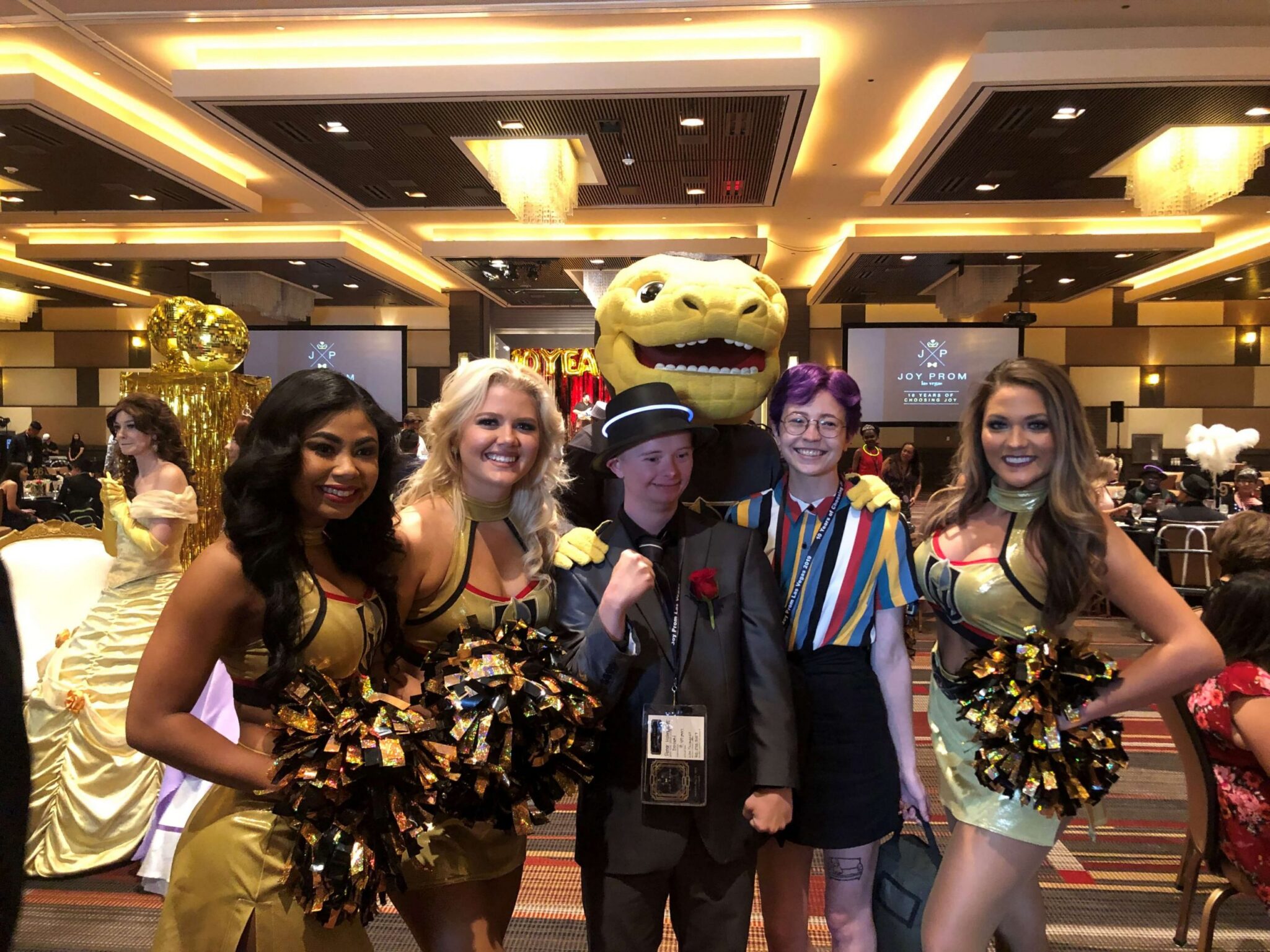 Group photo at a Las Vegas Joy Prom event, with attendees including cheerleaders, mascot, and special guests, highlighting the law firm's community engagement in accident and injury support.
