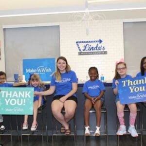 A photo of a man from a Las Vegas personal injury law firm, accompanied by children and adults, all wearing Make-A-Wish t-shirts and holding signs that say "Thank You" from Make-A-Wish, in front of a "Linda's Wishing Counter."