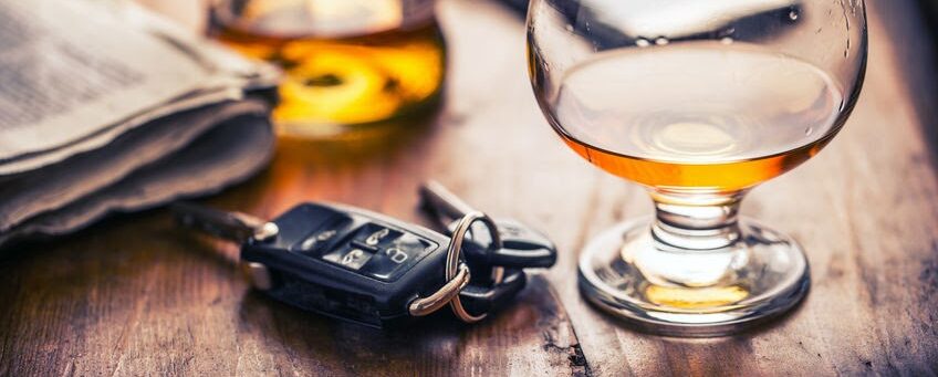 A close-up image shows a glass of amber liquid beside a bottle and car keys, symbolizing the dangers of drunk driving and potential personal injury cases, relevant to a Las Vegas law firm.