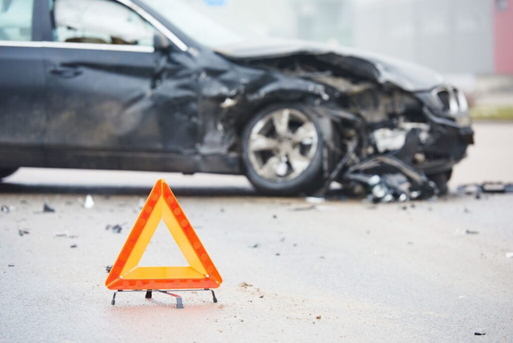 Scene of a car accident showing a damaged black vehicle with deployed hazard lights in the foreground, suggesting a potential personal injury case.