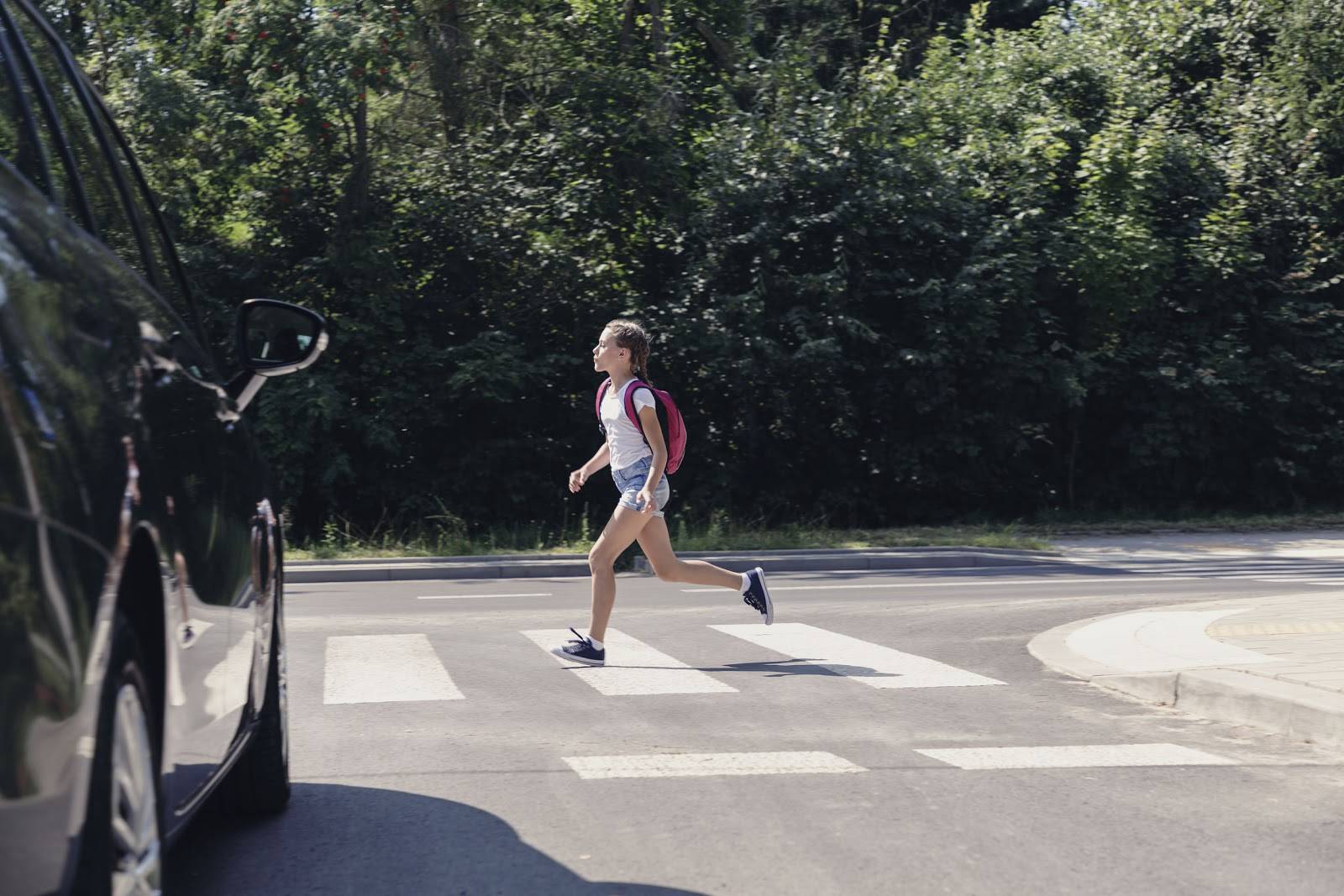 A young girl with a backpack is seen running across a crosswalk near a car, highlighting the potential dangers of pedestrian accidents and the need for legal assistance in Las Vegas for personal injury claims.