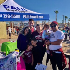 A group of people stands near a law firm booth at a Las Vegas community event, promoting personal injury legal services.
