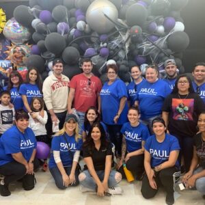 A group photo featuring the Paul Law Firm team, possibly at a community event in Las Vegas, with balloons and a festive atmosphere, supporting personal injury clients.