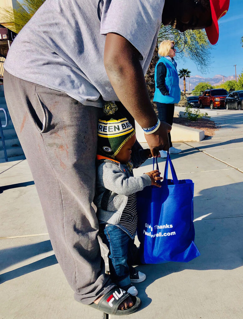 Image of a father and child, holding a blue Paulwell.com bag, symbolizing community support, potentially related to a personal injury law firm's outreach.