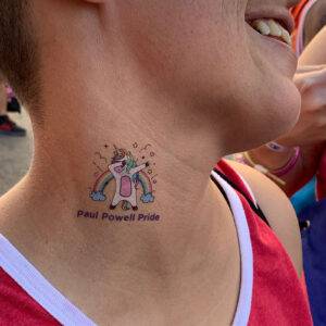 Close-up of a smiling person with a "Paul Powell Pride" unicorn temporary tattoo on their neck, representing inclusivity and support, relevant for a personal injury law firm in Las Vegas demonstrating community involvement.