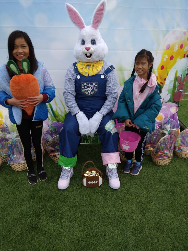 This image shows two smiling girls with the Easter Bunny, surrounded by Easter baskets in a vibrant outdoor setting, promoting a safe and joyful Easter while subtly connecting with the firm's commitment to protecting community members in Las Vegas.