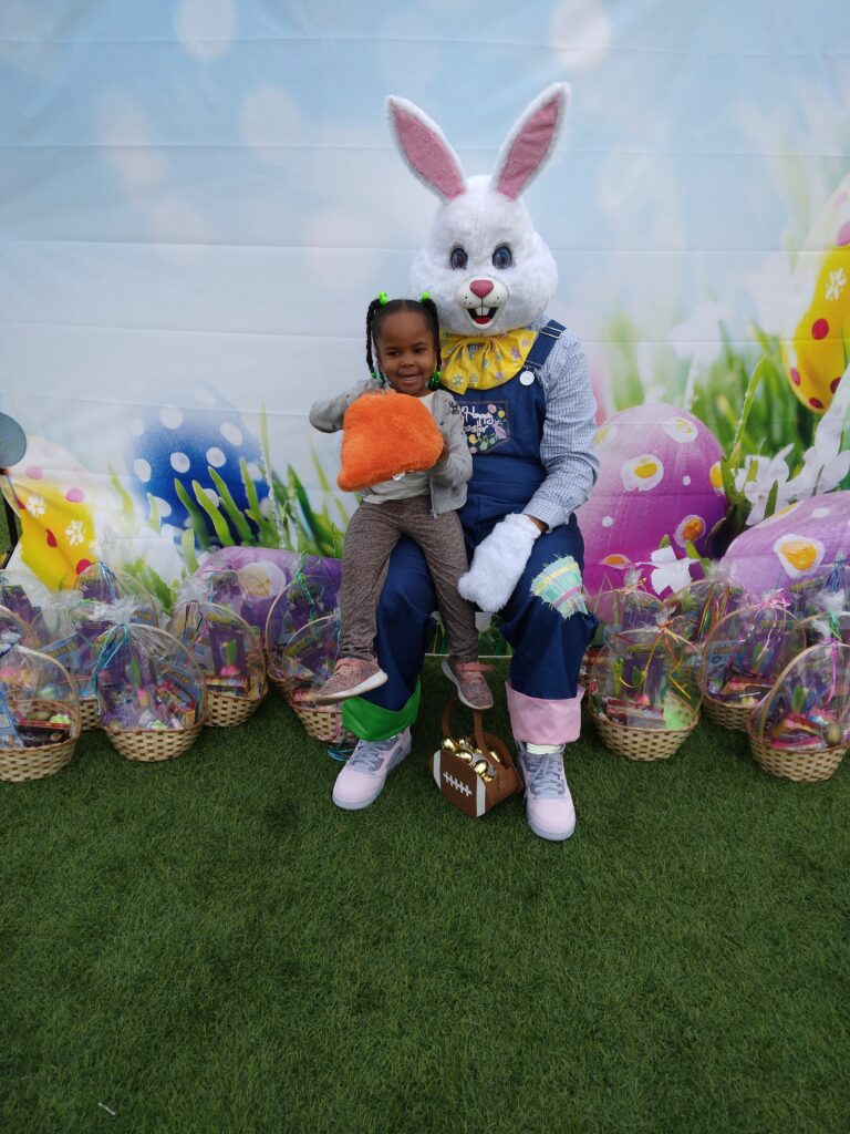 A young girl sits on the Easter Bunny's lap holding a carrot at a Las Vegas event surrounded by Easter baskets, ideal for community outreach and family personal injury legal services.
