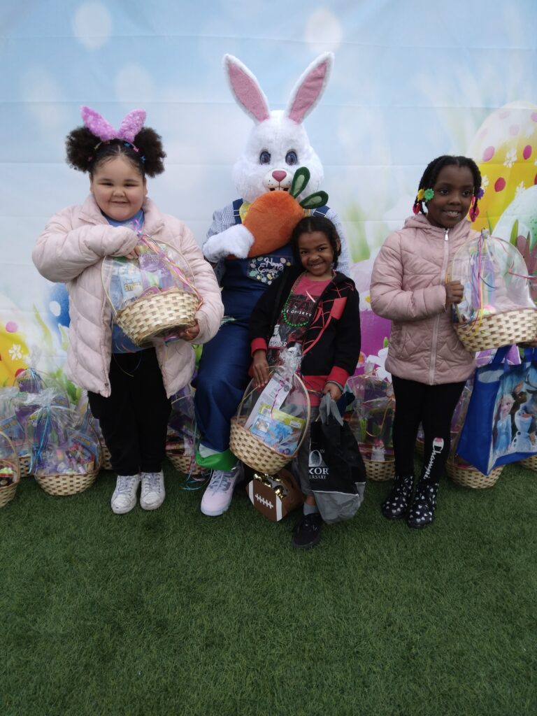 Three smiling young girls pose with the Easter Bunny and Easter baskets, with an Easter-themed backdrop, promoting a Las Vegas law firm and community engagement.