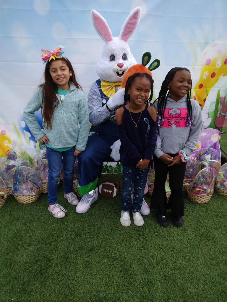 Three smiling girls pose with the Easter Bunny at a Las Vegas community event hosted by a personal injury law firm, with Easter baskets and a festive backdrop.