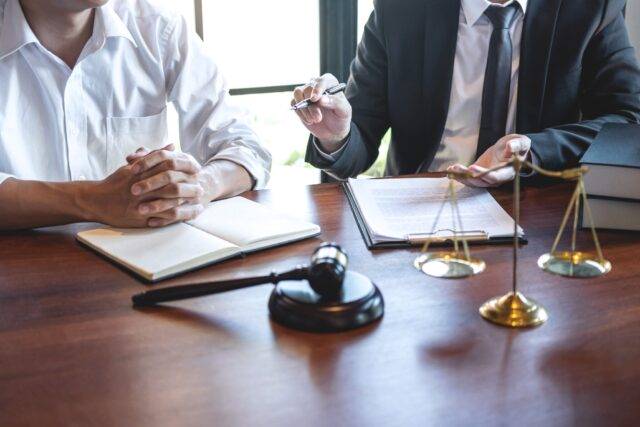 Image shows a lawyer discussing legal documents with a client at a wooden desk, with a gavel and scales of justice symbolizing law and fairness in personal injury cases.