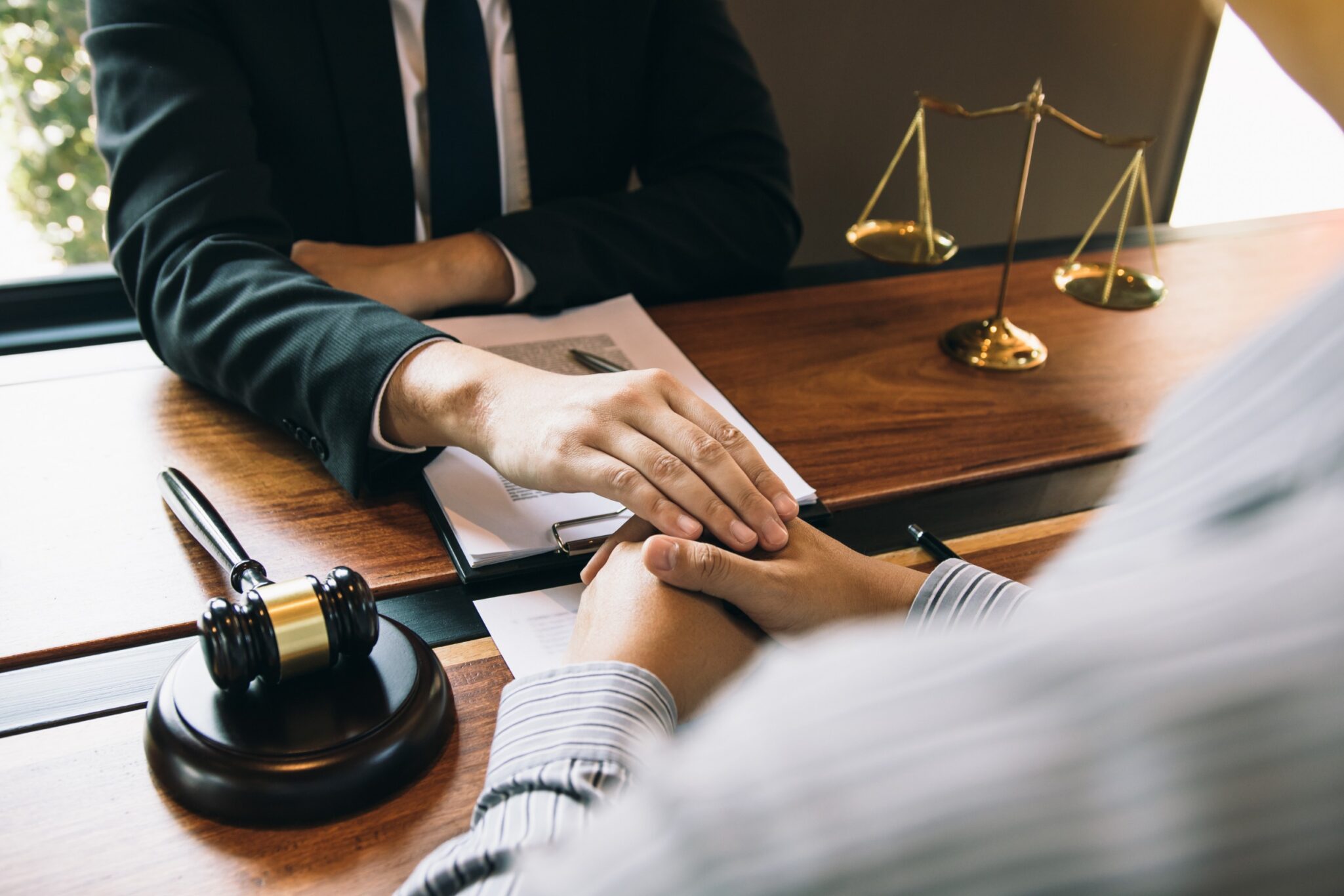 Close-up of a lawyer comforting a client, with hands gently placed on theirs, in a Las Vegas law office setting with a gavel and scales of justice, representing empathy and legal support for personal injury cases.