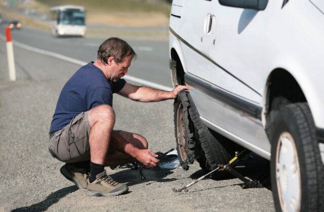 Man changing a flat tire on the side of a road, highlighting the risks of roadside accidents and the need for personal injury legal assistance in Las Vegas.