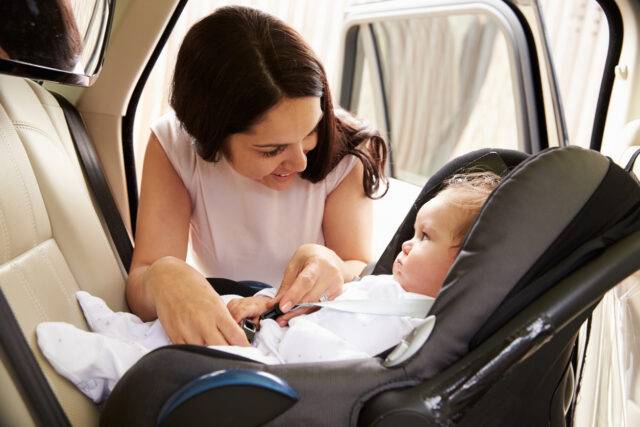 A mother secures her baby in a car seat inside a car, emphasizing the importance of child safety in vehicles, relevant for personal injury law in Las Vegas.