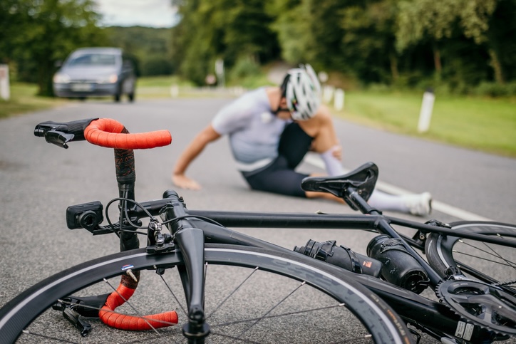 A cyclist lies injured on the road next to his bike after a collision with a car, emphasizing the need for legal assistance with personal injury claims.